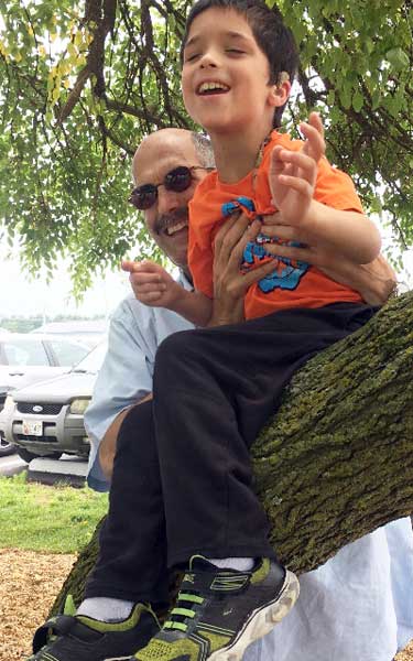 shows a boy sitting in a tree, with a volunteer nearby.