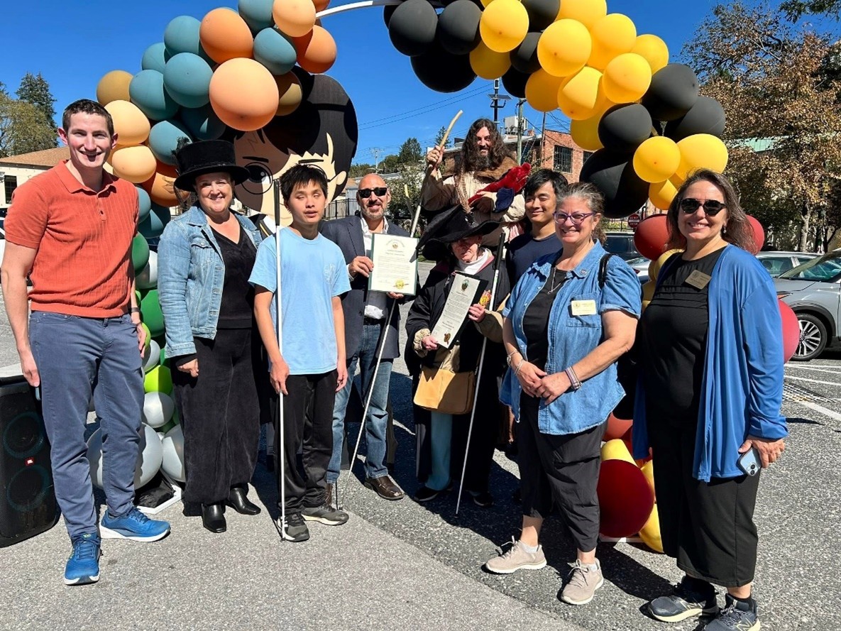 Ten people of blind and non-blind people of different ages and races smile together with commemorative award under a balloon arch